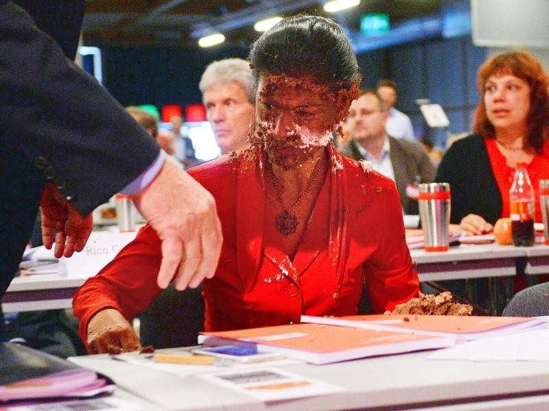 Die Aktivisten gingen an Wagenknecht vorbei, die in der ersten Reihe der Parteitagshalle saß und warfen ihr die Torte direkt ins Gesicht.