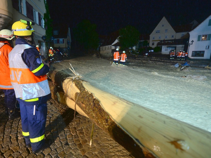 Sie kämpfen sich durch Schlamm und Wasser auf einer Überfluteten Straße, um zu den Häusern auf der gegenüberliegenden Seite zu gelangen.