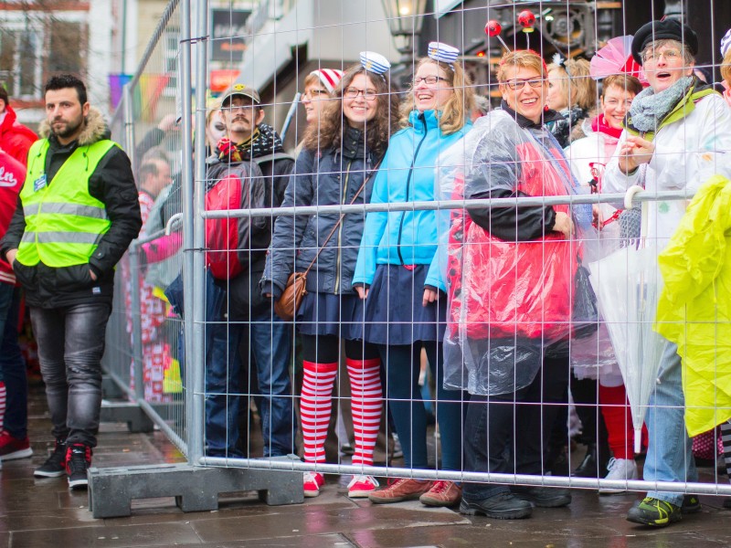 Närrinen stehen auf dem Alter Markt in Köln hinter einer Absperrung. Im Rheinland und anderswo beginnt an Weiberfastnacht oder Altweiber der Straßenkarneval unter verstärkten Sicherheitsvorkehrungen.