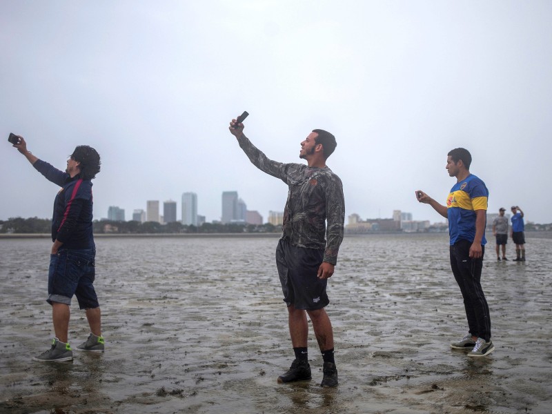 The Tampa skyline is seen in the background as local residents (L-R) Rony Ordonez, Jean Dejesus and Henry Gallego take photographs after walking into Hillsborough Bay ahead of Hurricane Irma in Tampa, Florida, U.S., September 10, 2017. REUTERS/Adrees Latif