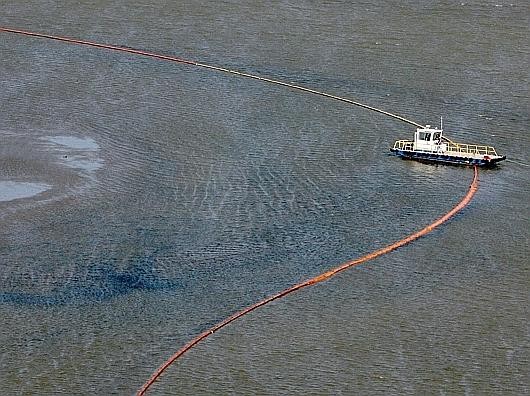 Ein Schiff legt Ölbarrieren aus.