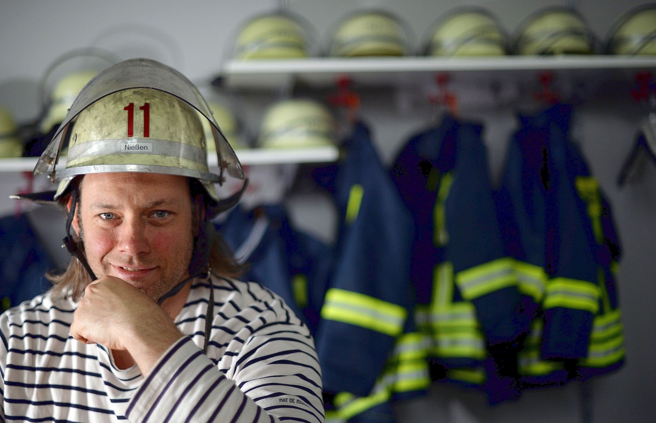 Jörg Nießen mit Feuerwehrhelm im Umkleideraum.