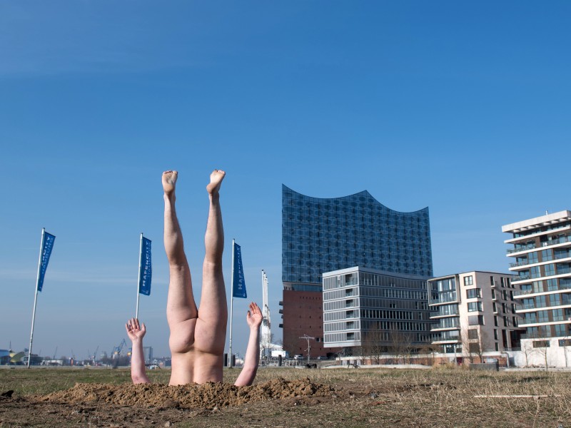 Ja, hier steckt ein Mann kopfüber und nackt in der Erde – vor der Hamburger Elbphilharmonie. Die Aktion des russischen Konzeptkünstlers Andrey Kuzkin ist Teil der Serie „The Phenomenon of Nature or 99 Landscapes with Trees“ (Das Phänomen der Natur oder 99 Landschaften mit Bäumen). Wir zeigen weitere aufsehenerregende Aktionen von Künstlern.