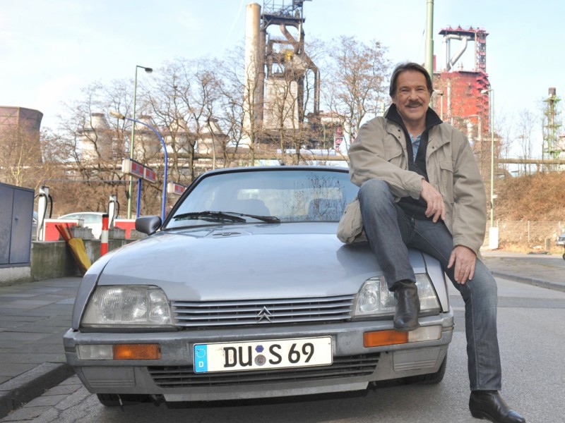 Götz George mit seinem legendären Dienst-Citroen vor Duisburger Kulisse.