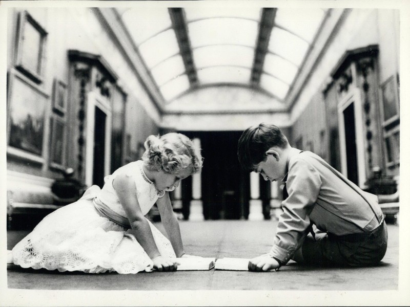 Lesend sitzen die Geschwister am achten Geburtstag von Charles in der Kunstgalerie des Buckingham Palace. Noch sind die beiden allein, aber im Jahr 1960 bekommen sie einen weiteren Bruder, Prince Andrew Albert Christian Edward, Duke of York sowie im Jahr 1964 Prince Edward Antony Richard Louis, Earl of Wessex.