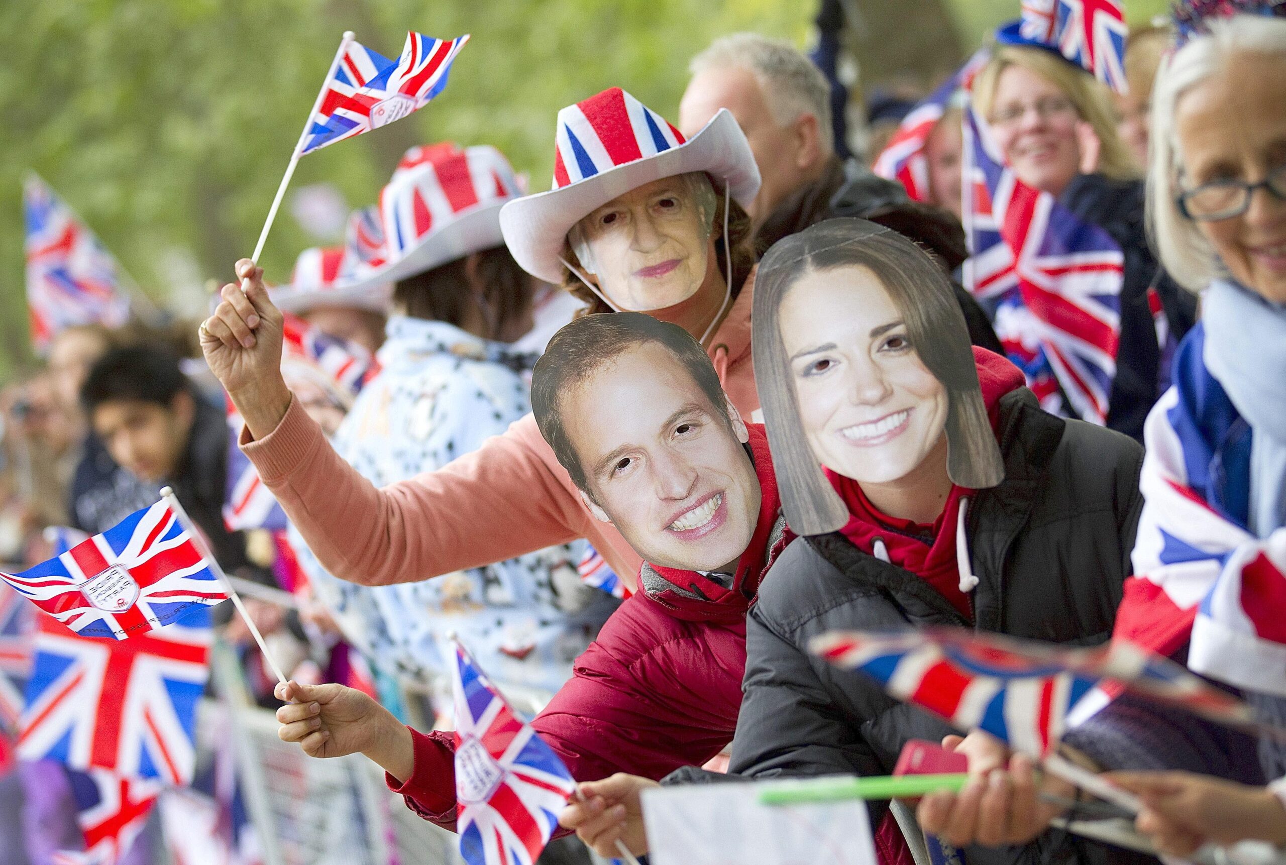 Fans des Hochzeitspaares tragen Masken und schwingen Union Jack-Fähnchen.