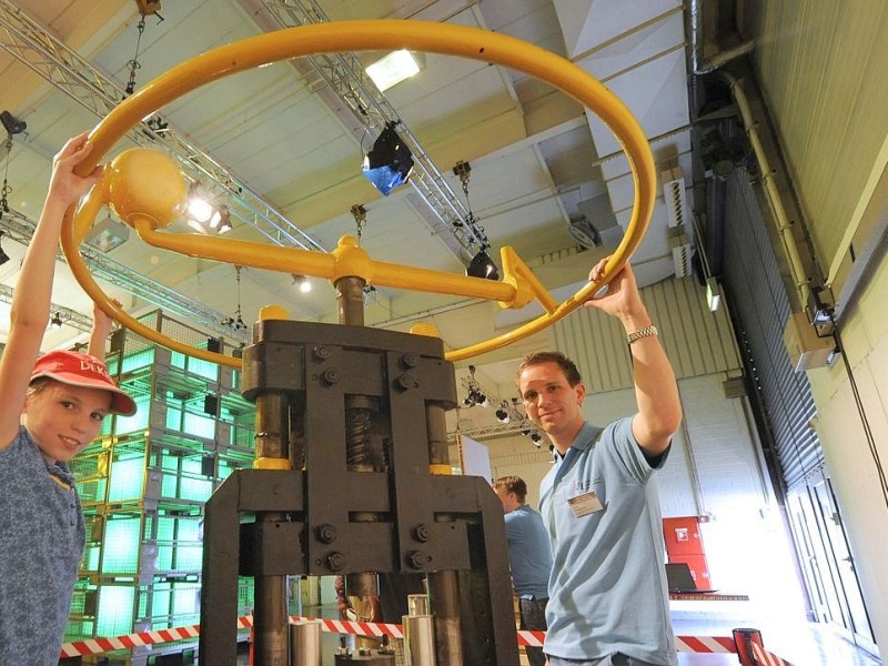 Stefan Ossenkemper vom Institut für Umformung und Leichtbau unterstützt Besucherin Christina (11) an der Handspindelpresse bei der Herstellung eines Chips für Einkaufswagen.