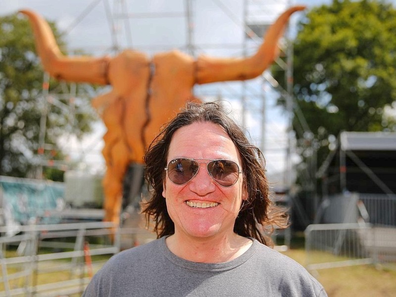 Thomas Jensen, Gründungsmitglied des Wacken-Open-Air-Festivals, steht vor dem Logo des Festivals.