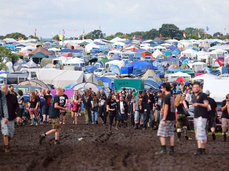 Besucher des Wacken-Open-Air-Festivals laufen über die verschlammten Wege des Festivalgeländes.