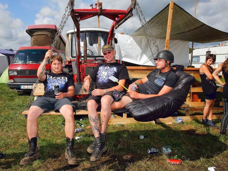 Besucher des Wacken-Open-Air-Festivals sitzen in einer zum Sofa umgebauten Treckerschaufel auf dem Festivalgelände.