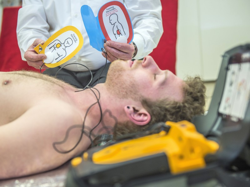 Ist die Bewusstlosigkeit festgestellt, klappt man den Defibrillator (AED) auf, der einen anleitet. Zunächst setzt man den Notruf ab und klebt die Elektroden auf.