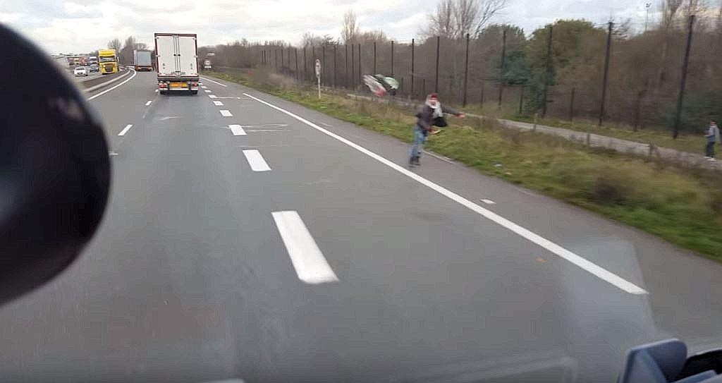 Ein Mann am Straßenrand wirft eine leere Plastikflasche nach dem Lkw, nachdem der Fahrer zuvor gezielt auf Flüchtlinge losgefahren war. 