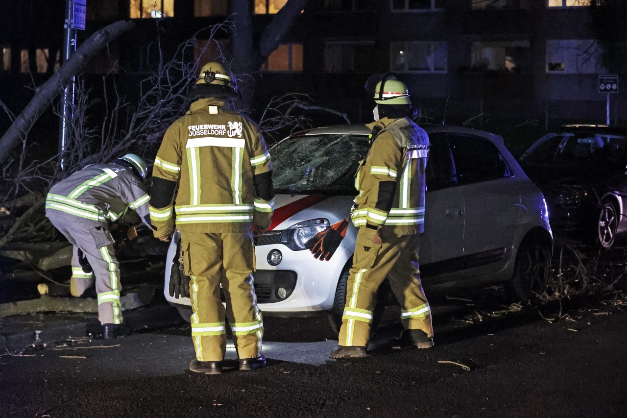 Düsseldorf: Im Ortsteil Wersten arbeiten Feuerwehrleute an einem Pkw, der unter einem Baum liegt, der vom Sturm umgerissen wurde. Der Baum riss bei seinem Sturz auch eine Gaslaterne um, so dass am Unfallort Gas ausströmte. 