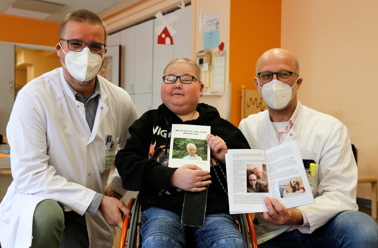 Prof. Dr. Dominik Schneider (Direktor der Klinik für Kinder- und Jugendmedizin), Fynn und Dr. Benedikt Bernbeck (Oberarzt im Westfälischen Kinderzentrum) präsentieren das Buch des 13-Jährigen.