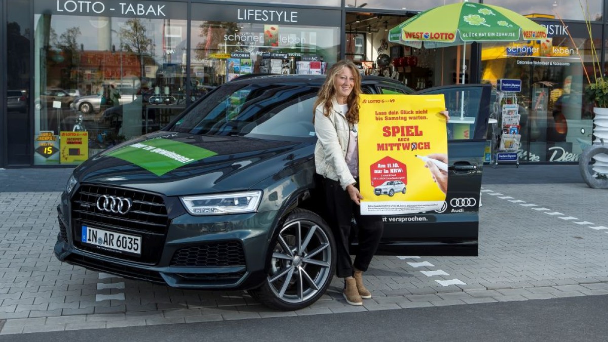 WestLotto-Annahmestellenleiterin Hildegard Kerkhoff-Kemper freut sich auf die Sonderauslosung und präsentiert vor ihrem Geschäft das Fahrzeug. 