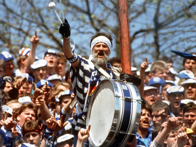 Catweazle:
Karl-Heinz Olschewski stand 28 Jahre lang mit seiner Trommel in Block 5 des Parkstadions angelehnt am Lautsprechermast. Den Namen Catweazle bekam das Original mit Rauschebart aufgrund seiner Ähnlichkeit zum Hauptdarsteller einer Serie aus den 70ern. Der Trommler heizte den Schalkern auf der Tribüne ein, egal ob Schalke in den 80ern in der zweiten Liga spielte oder 1997 den Uefa-Cup holte. In der Arena auf Schalke war Catweazle nicht mehr zu sehen, auch weil Schalke seinen Antrag auf einen Masten im Block aus Sicherheitsgründen ablehnte. 2013 verstarb Karl-Heinz Olschewski. Einen Gruß für die Fans in der Arena hat er aber hinterlassen:
„Diese ganzen Mode-Fuzzis, diese Sesselfurzer, ‚sehen und gesehen werden’ - da lach ich mich kaputt. Im VIP-Raum sitzen Leute mit Fliege, da krieg ich ein am Rappel .“