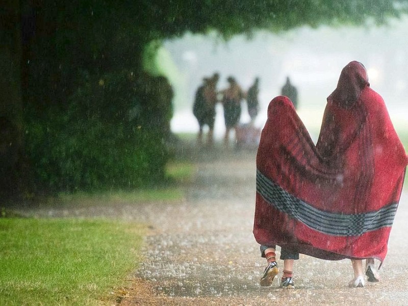 Zwei Kinder gehen mit einer Decke als Regenschutz durch eine Allee in Hannover.