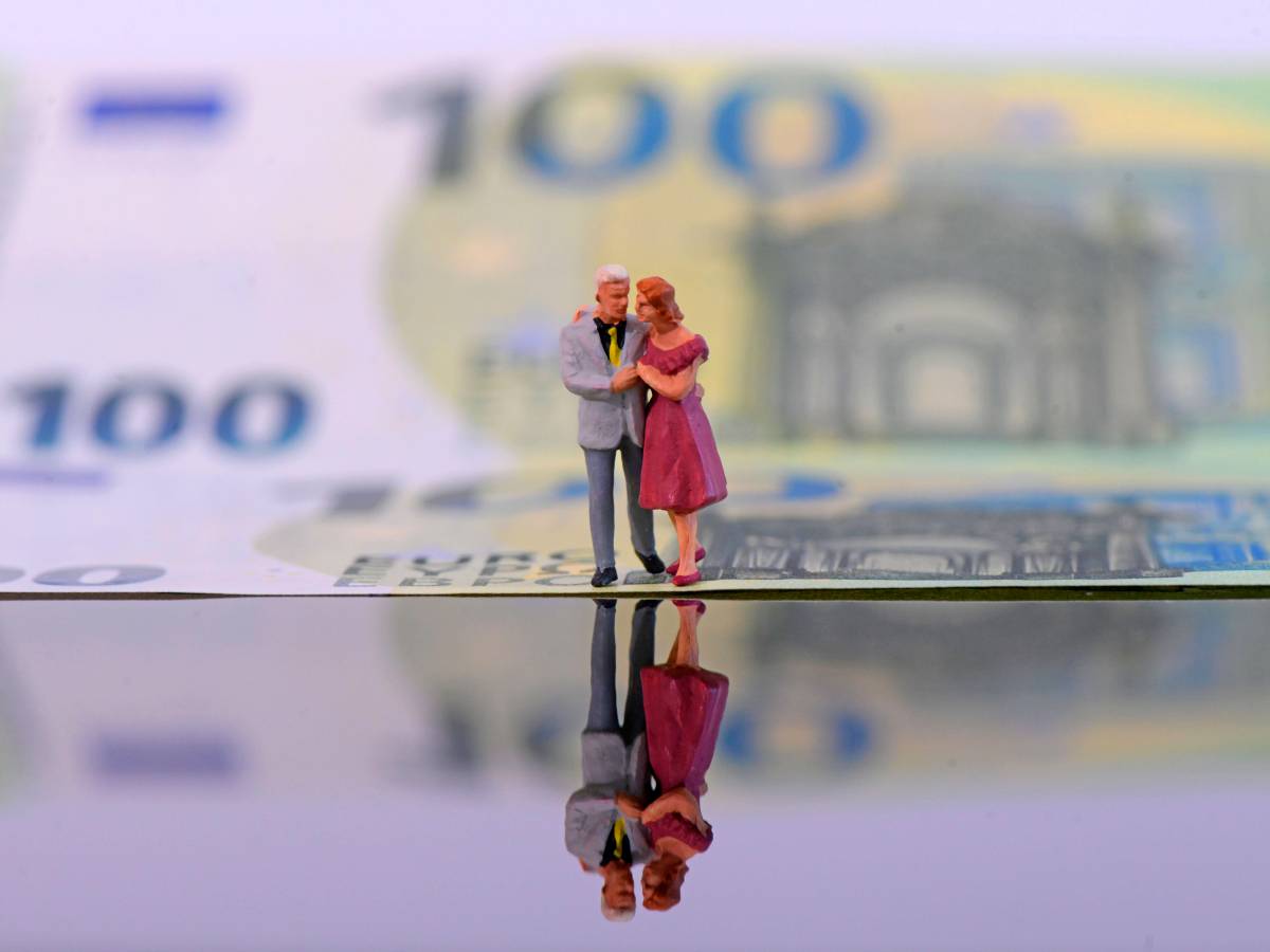 Ein Ehepaar umarmt sich vor der Kulisse eines 100-Euro-Scheins.