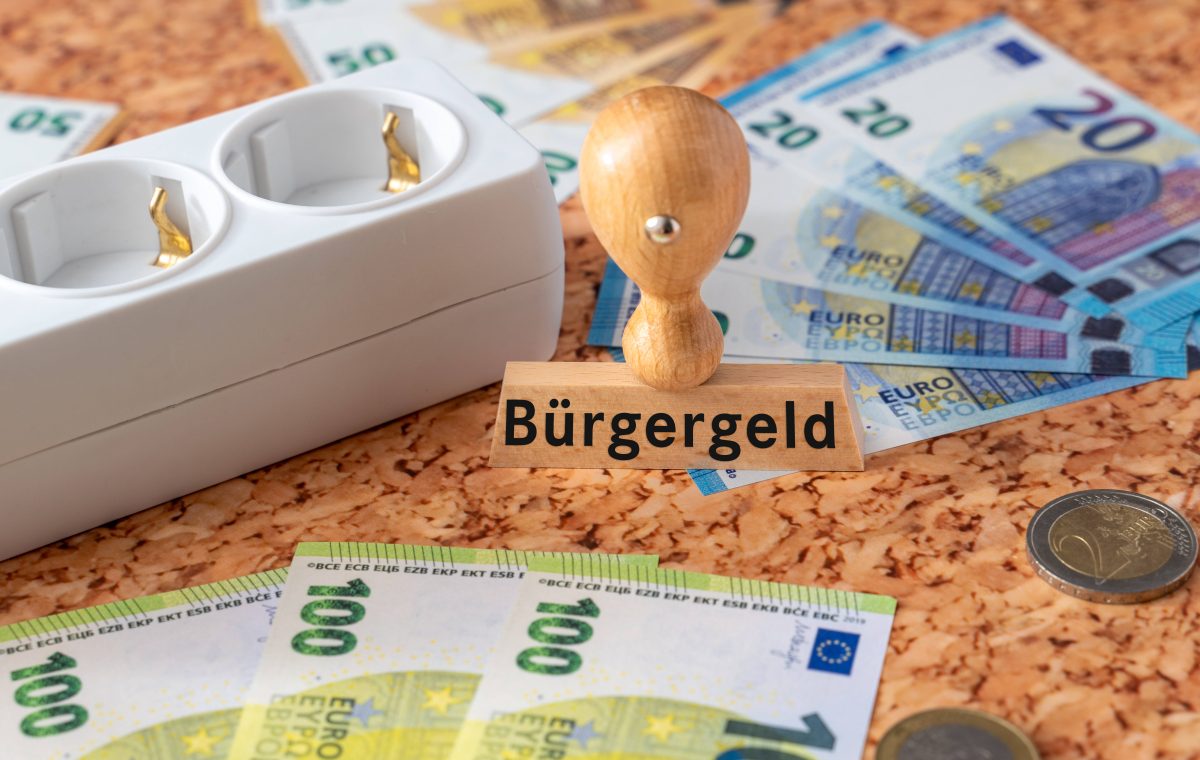 Ein Stempel mit dem Aufdruck Bürgergeld sowie viele Euro-Geldscheine und eine Steckdosenleiste.