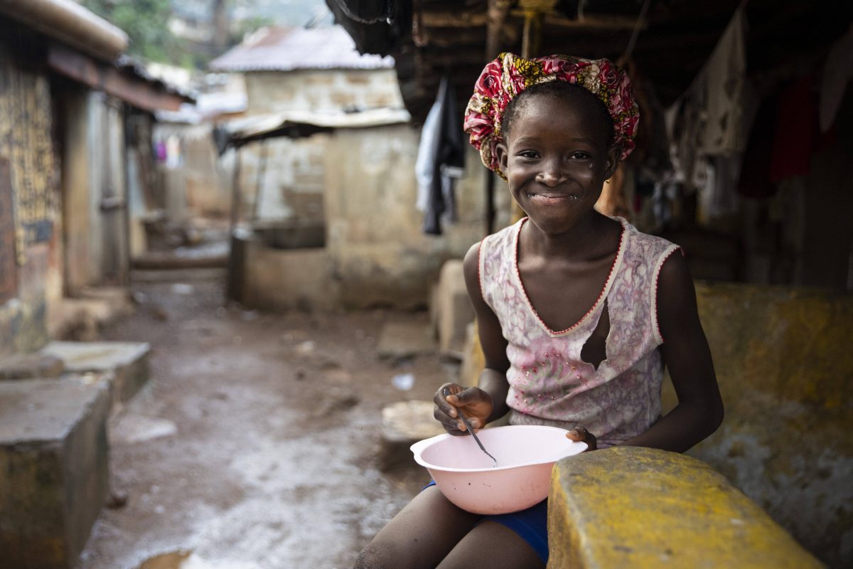 Ein Mädchen, das, mit einem Teller in Bomeh Village auf der Kissy-Road-Müllkippe sitzt und dort lebt.