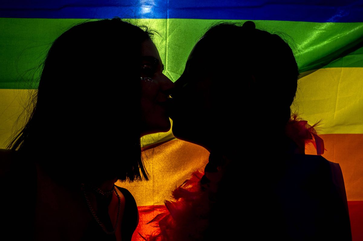 Zwei Frauen küssen sich vor einer Pride-Flagge