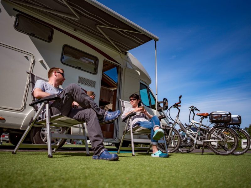 Paar sitz auf Rasen vor Camper auf Campingplatz im Urlaub