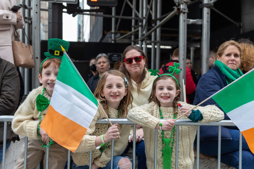 Junge Mädchen stehen an einem Absperrzaun und halten anlässlich von Feierlichkeiten zum St. Patrick's Day eine irische Fahne in der Hand.