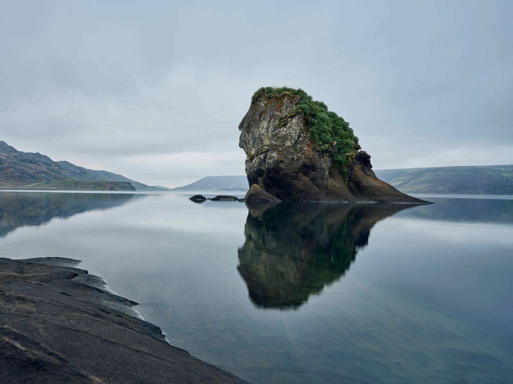 Ein Fels steht inmitten eines Sees in Island.