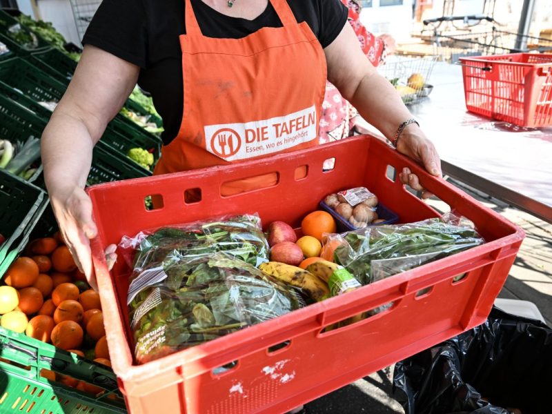 Tafel-Mitarbeiterin hält Kiste mit Obst und Gemüse hoch