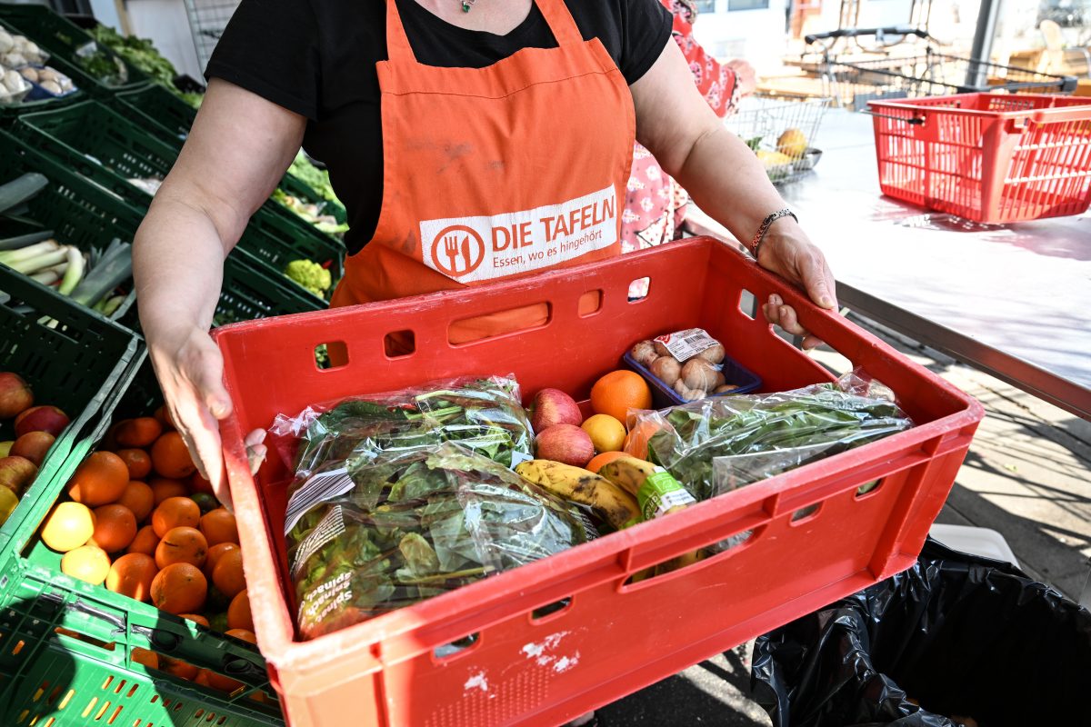 Tafel-Mitarbeiterin hält Kiste mit Obst und Gemüse hoch