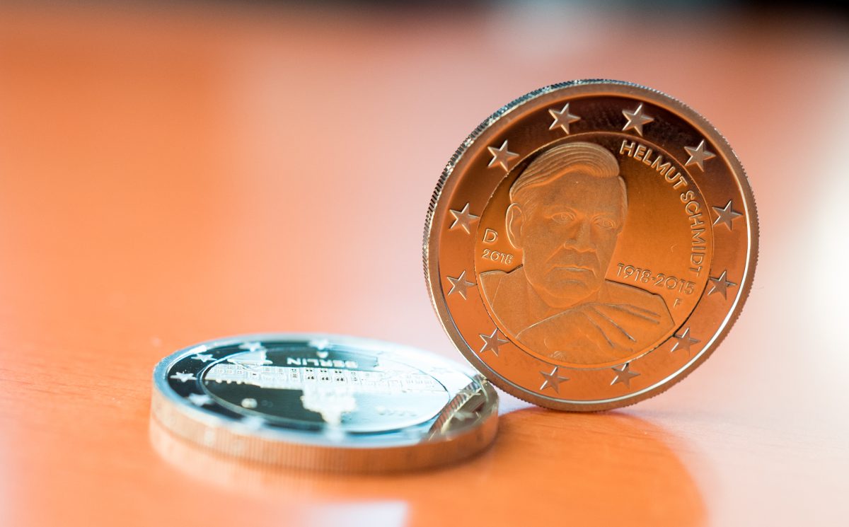 Eine 2-Euro-Münze mit Helmut Schmidt steht auf dem Rand. Daneben liegt eine 2-Euro-Münze "Berlin".