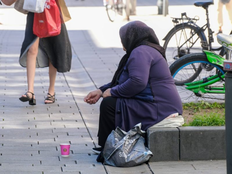 Frau sitzt auf der Straße und bettelt