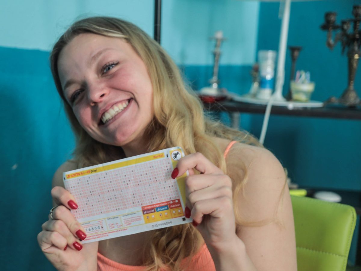 Eine Frau hält freudestrahlend einen Lottoschein in beiden Händen.
