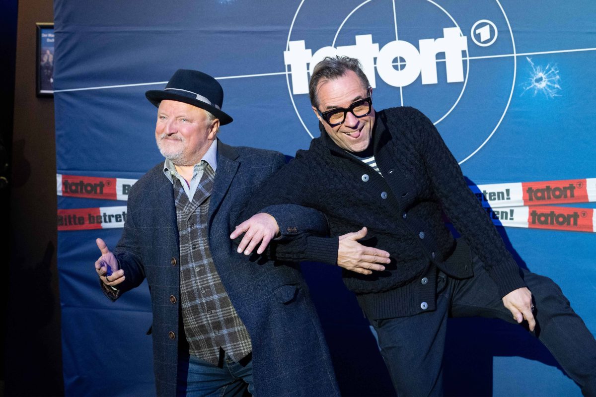 Schauspieler Axel Prahl und Jan Josef Liefers stehen vor einem blauen Hintergrund. Auf diesem Hintergrund steht in weiß "Tatort".