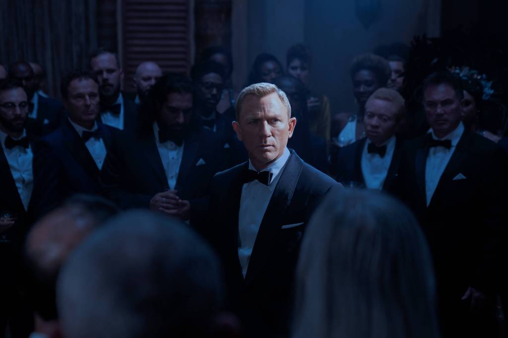 Daniel Craig im Anzug von anderen Anzugträgern umzingelt.