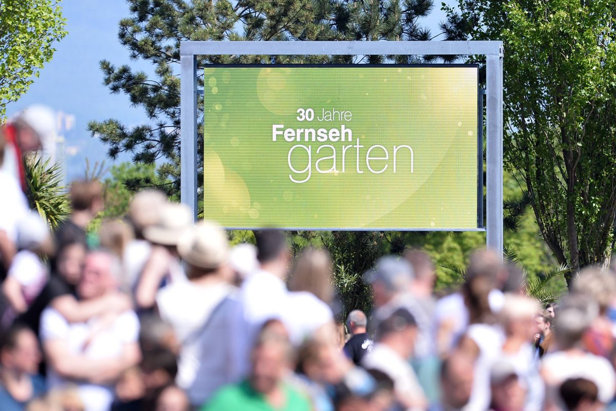 Auf dem Bild ist das Outdoor-Studio in Mainz vom ZDF-Fernsehgarten zu sehen. Verschwommen im Vordergrund ist das Publikum zu sehen. Gestochen scharf im Hintergrund ist eine Tafel in grün zu sehen.