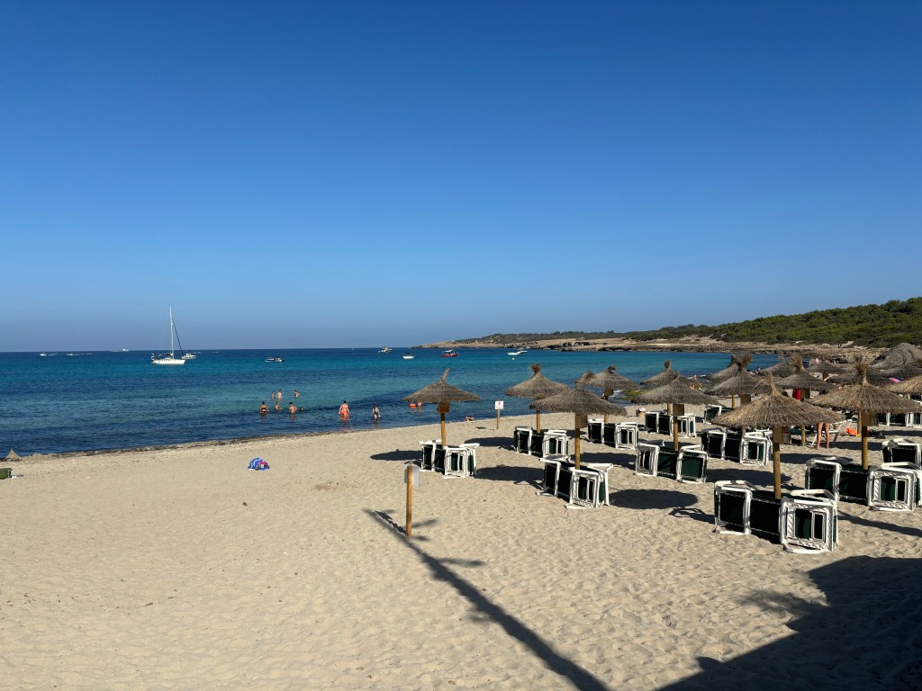 Menschen, die in der ruhigen Badebucht des Playa Oratori schwimmen und die Sonne genießen.