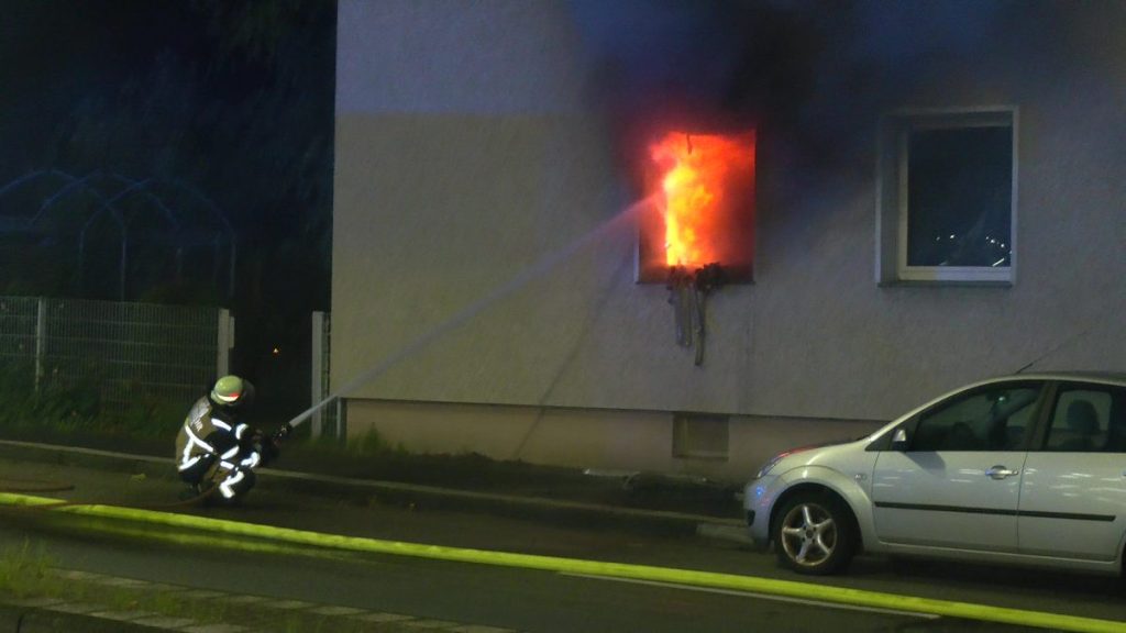 Wohnungsbrand in Essen: Ein Feuerwehrmann löscht von außen durch das zerstörte Fenster.